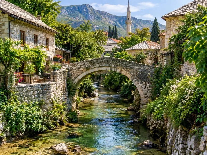 Die kleine steinerne Krumme Brücke in Mostar über einem schmalen, von Grün gesäumten Bach