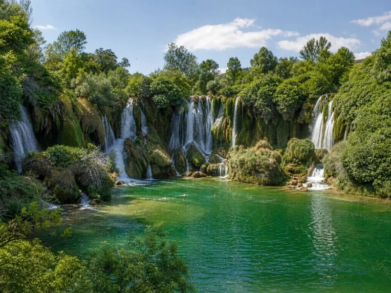 Close view of water falling over rock ledges at Kravica into a turquoise pool